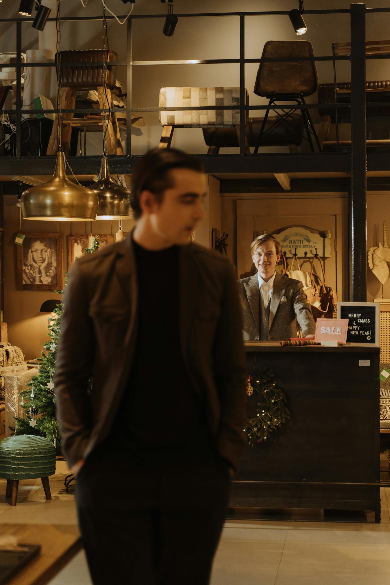 Warm indoor scene of a retail store featuring a customer and an employee behind the counter.